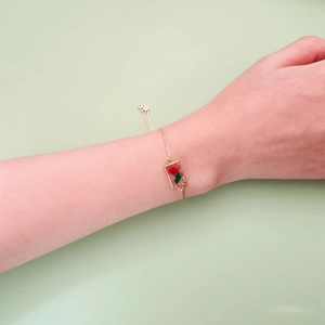 Détail d'un bracelet doré ajustable orné d'un pendentif avec une véritable fleur rouge