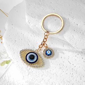 Golden Evil Eye keychain with blue enamel and sparkling rhinestones on stone surface
