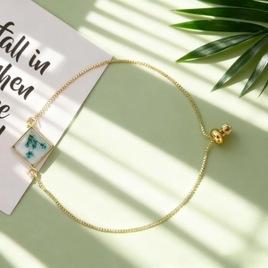 Détail du bracelet chaîne dorée avec fleur séchée bleue dans un pendentif en résine