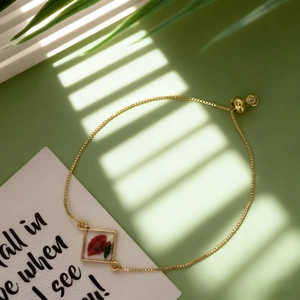 Détail d'un bracelet ajustable en chaîne dorée avec pendentif carré de fleurs séchées rouges