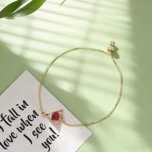Détail du bracelet réglable en or avec fleurs séchées rouges dans un cadre triangulaire