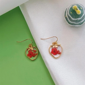 Dettaglio degli orecchini in resina a forma di fragola con veri fiori secchi rossi all'interno