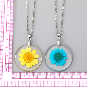 Détail de pendentifs ronds en résine faits main avec de vraies fleurs séchées et règle