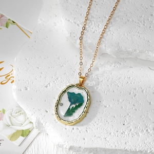 Détail du pendentif ovale en résine avec fleur séchée bleue et perle sur un cadre doré poli