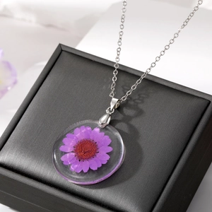 Gros plan d'une marguerite violette séchée en résine transparente avec sa chaîne argentée