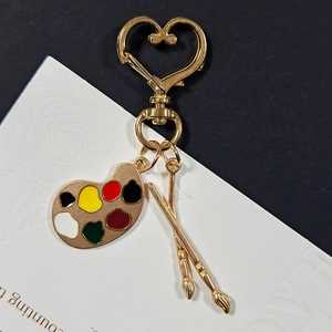 Detailed close-up of a golden palette and brushes keychain charm on a heart clasp