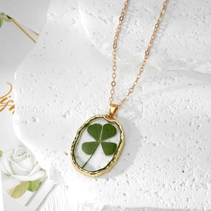 Collier élégant doré avec pendentif en résine de vrai trèfle sur un fond de pierre