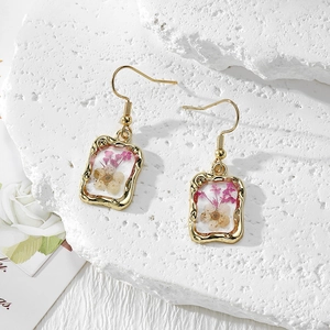 Elegant gold earrings with purple and white dried flowers preserved in transparent resin