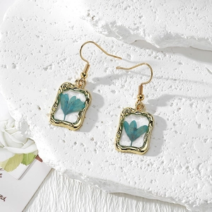 Detail of square gold earrings featuring blue dried flowers in transparent resin