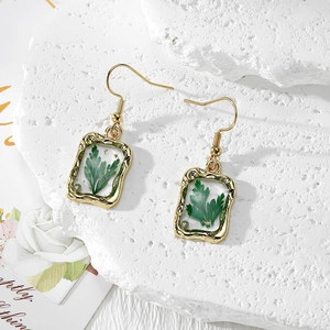Detailed close-up of handmade gold earrings with green dried flowers and gold foil accents