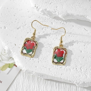 Detail of handmade gold earrings featuring red dried flowers in clear resin pendants