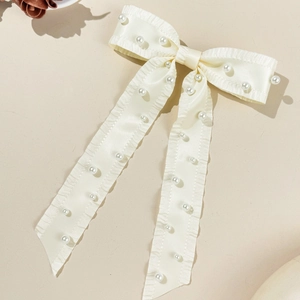 Detail of elegant beige satin bow hair clip with faux pearls and ruffled edges