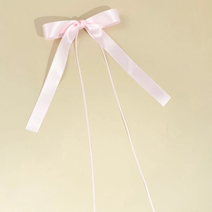 Detail of light pink satin bow hair clip with long ribbons on a clean beige background