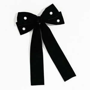 Close-up of black velvet bow hair clip with white pearls and long ribbons on white backdrop