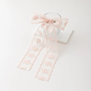 Elegant pink lace bow hair clip with long streamers on a white textured stone base