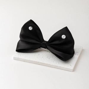 Détail d'une pince à cheveux nœud en satin noir avec perles sur socle en pierre