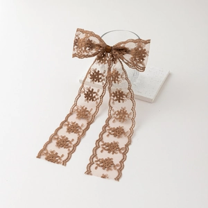 Detail of coffee brown lace bow hair clip with floral embroidery and long flowing ribbons