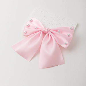 Détail d'une pince à cheveux avec nœud en satin rose orné de perles blanches élégantes