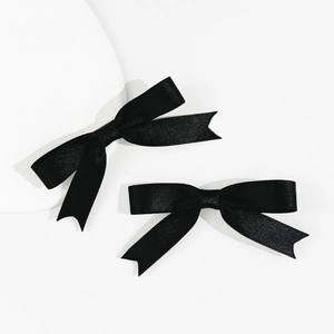 Detail of two black satin bow hair clips with soft silk texture and classic ribbon design