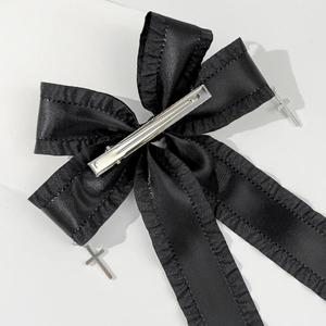 Detail of black gothic bow hair clip featuring satin ruffles and silver cross pendants