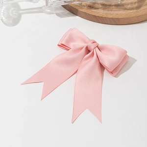 Detailed view of the pink satin bow hair clip on a minimalist wooden tray display