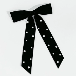 Detail of elegant black velvet bow hair clip featuring hand-sewn pearls on a white surface