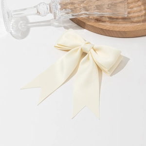Elegant cream satin bow hair clip for women with classic swallowtail design on wooden plate