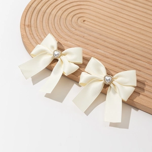 Elegant cream satin bow hair clip with pearl heart center on a decorative wooden tray