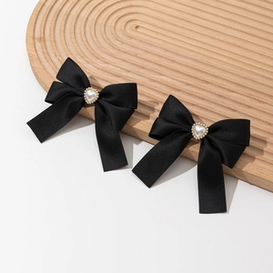 Detailed view of black satin bow hair clips featuring gold-edged heart pearls on wood