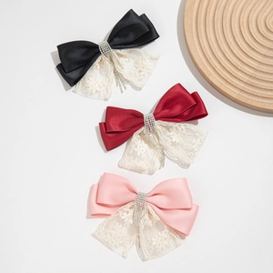 Close-up of satin bow hair clips with white lace trim and dangling rhinestone tassels