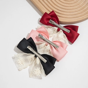 Detail of three satin bow hair clips in red, pink, and black with lace flower layering