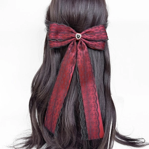Macro detail of a dark Lolita hair clip featuring red satin, black lace, and a heart rhinestone