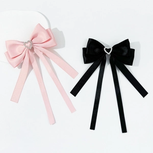 Détail de barrettes à nœuds en satin rose et noir avec strass en forme de cœur