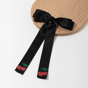 Detail of black satin bow hair clip with long ribbons and red cherry print pattern