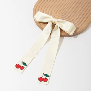 Elegant cream satin bow hair clip with red cherry prints on long ribbons over wood