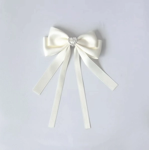 Détail d'une pince à cheveux nœud en satin crème avec strass en forme de cœur argenté