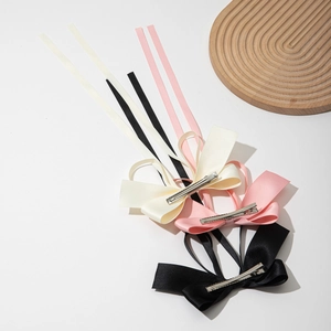 Close-up of three long satin ribbon bow hair clips in cream, pink and black colors