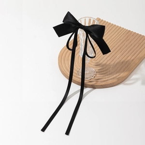 Elegant black silk satin bow hair clip with long ribbons on a wavy wooden tray
