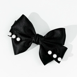 Détail de la pince à cheveux noeud en satin noir ornée de perles blanches sur fond blanc