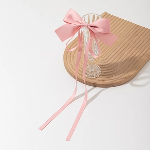 Elegant pink satin bow hair clip with long ribbons draped on a crystal glass rim
