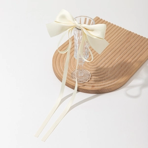 Elegant cream satin bow hair clip with long ribbons on a minimalist glass display
