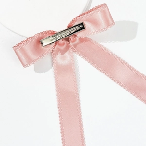 Détail du nœud en soie rose avec bords en dentelle ondulée et pince crocodile en métal argenté