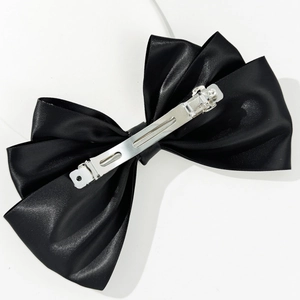 Detail view of the silver metal spring clip and black satin fabric on oversized bow hairpin