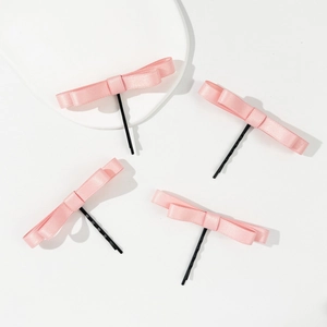 Lot de quatre barrettes en satin rose avec épingles en métal noir sur plateau blanc