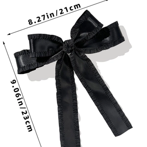 Detail view of a large black satin bow hair clip with ruffle edges and size markings