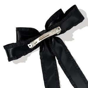 Detail of black satin bow hair clip with ruffle edges and silver metal spring fastener