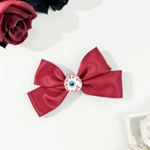 Gothic Halloween hair clip with dark red bow and realistic eyeball detail on white surface