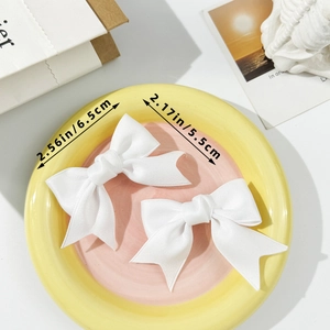 Set of two white ballet-style bow hair clips on a decorative ceramic plate