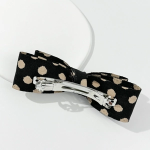 Close-up of black polka dot bow hair clip with textured ribbon and silver metal spring clip