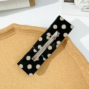 Close-up of a rectangular hair clip with beige polka dots on black fabric and metal clip